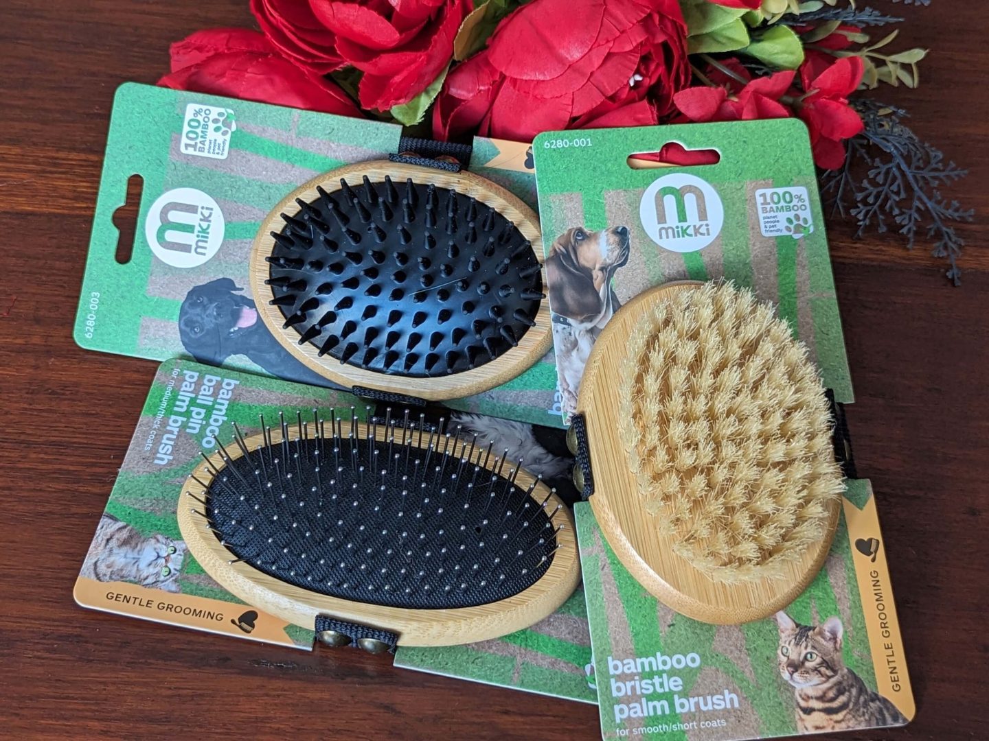 Bamboo palm pet brushes from Mikki displayed against a wooden background with red flowers beside for the something you need section of the four gift rule Christmas gift guide