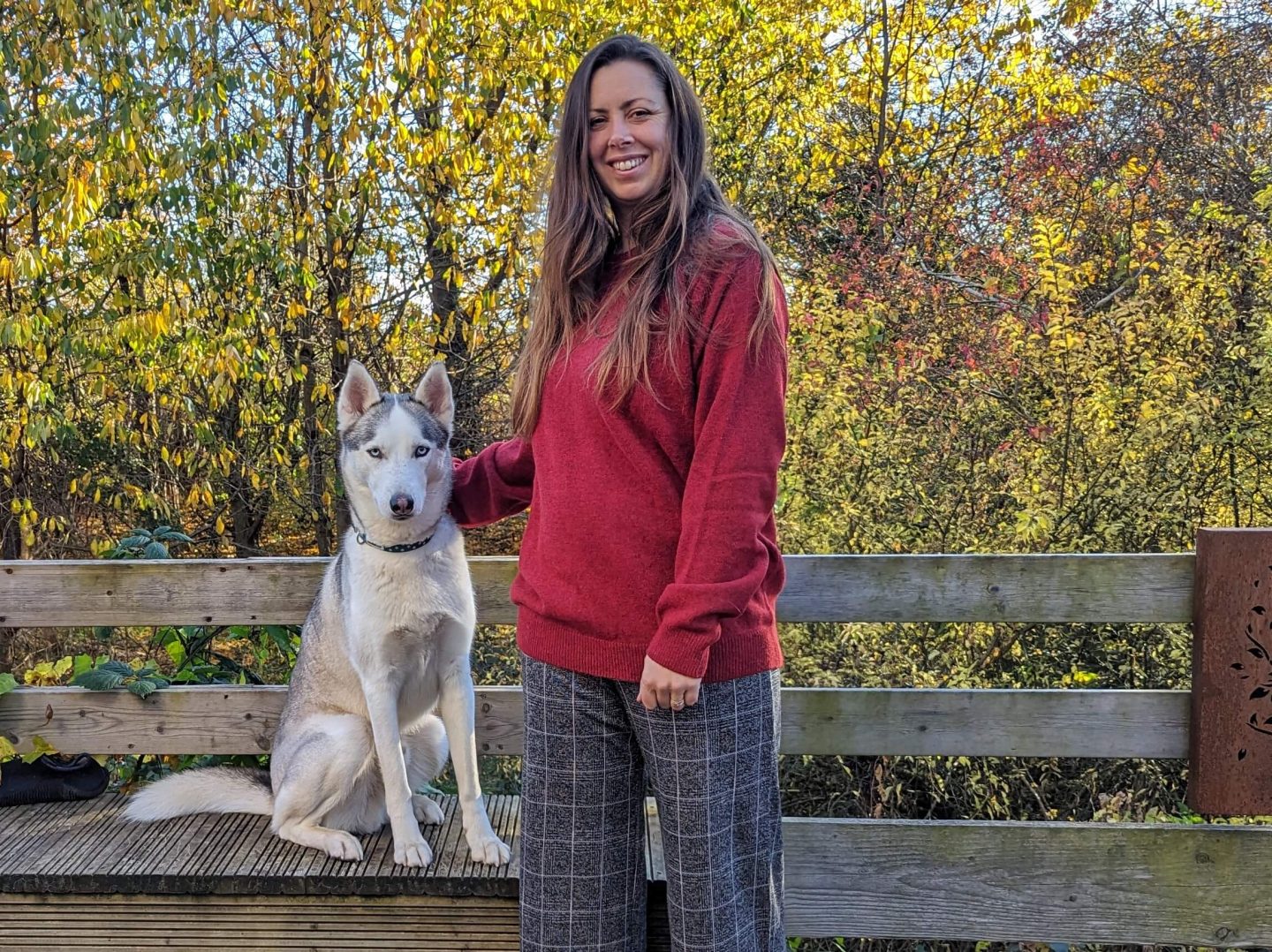 Natalie wearing a crimson Cotton Traders jumper standing next to Marko with autumn trees behind
