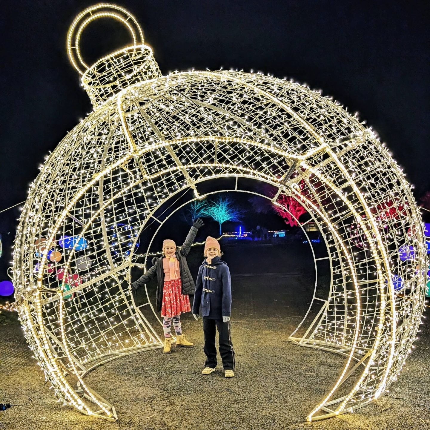 Two girls standing inside a bauble made of white lights on Winter Glow light trail 2024 at the Three Counties Showground in Malvern, Worcestershire