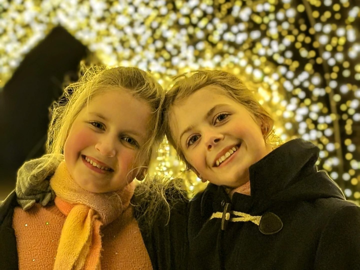 Two girls in warm clothing posing in a light tunnel at Winter Glow in Malvern, Worcestershire Christmas 2024