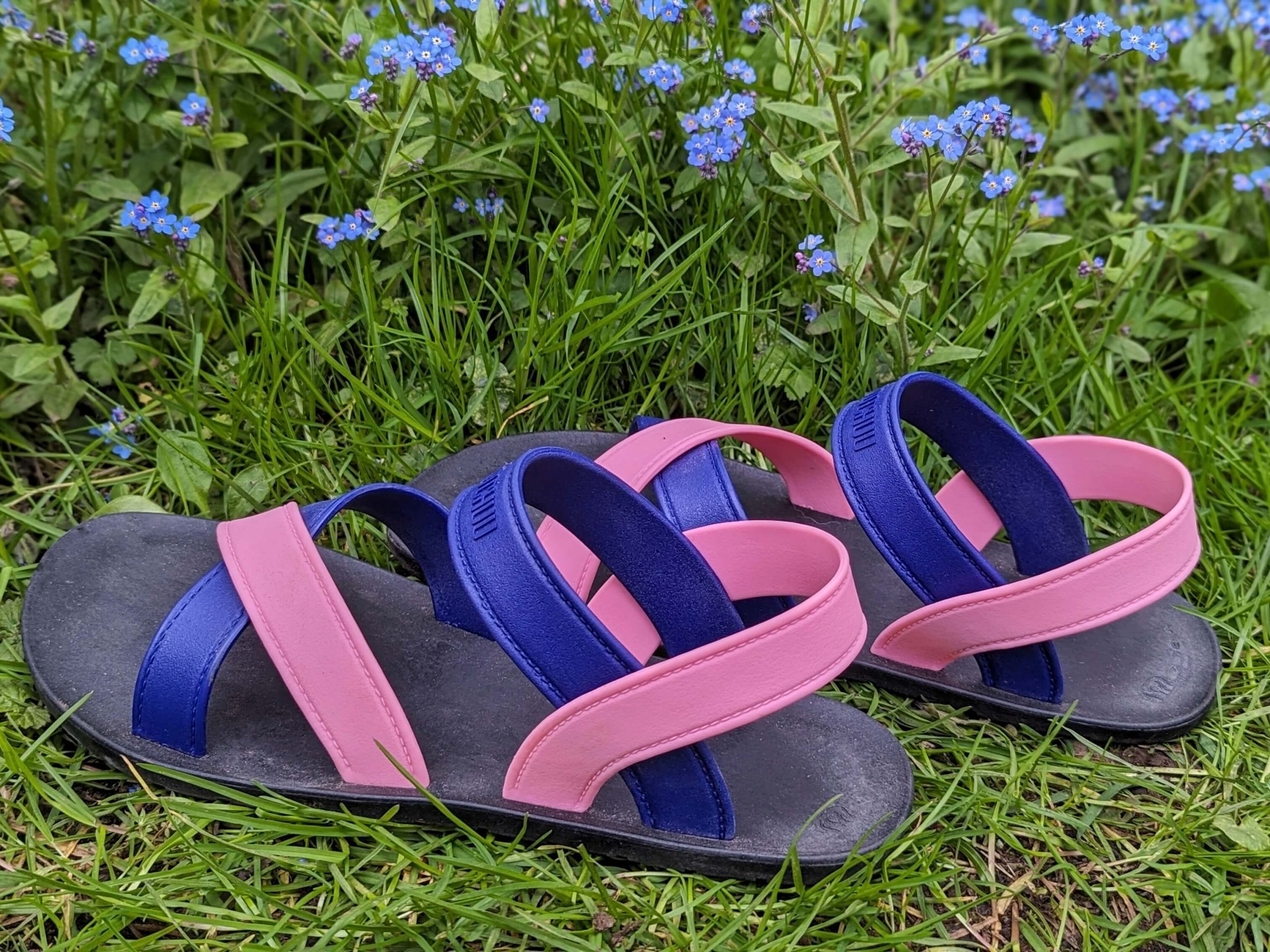 Pink and blue MOO CHUU sandals with black soles displayed on grass