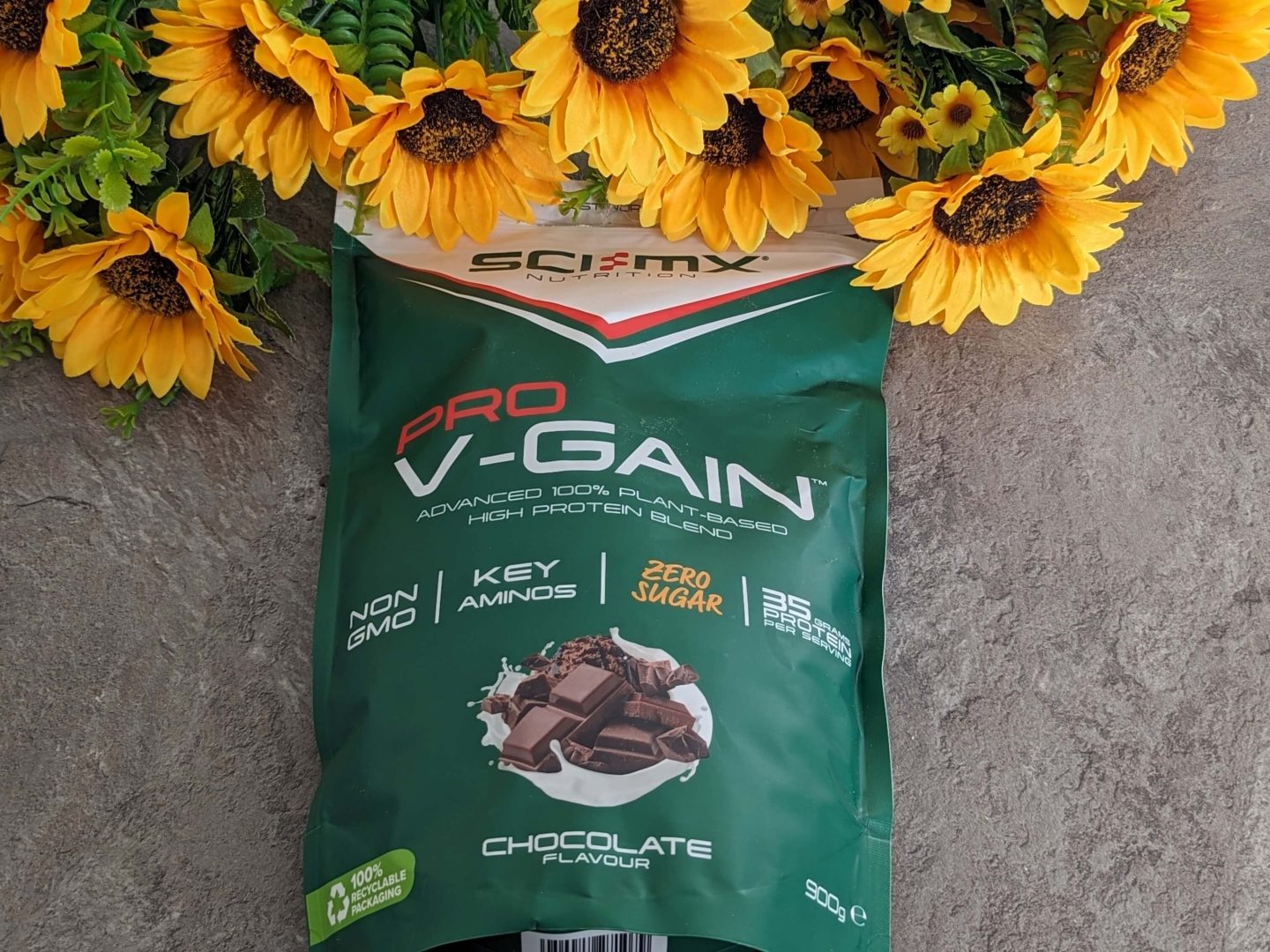 Packet of V-Gain chocolate flavour protein shake displayed against a bunch of sunflowers.