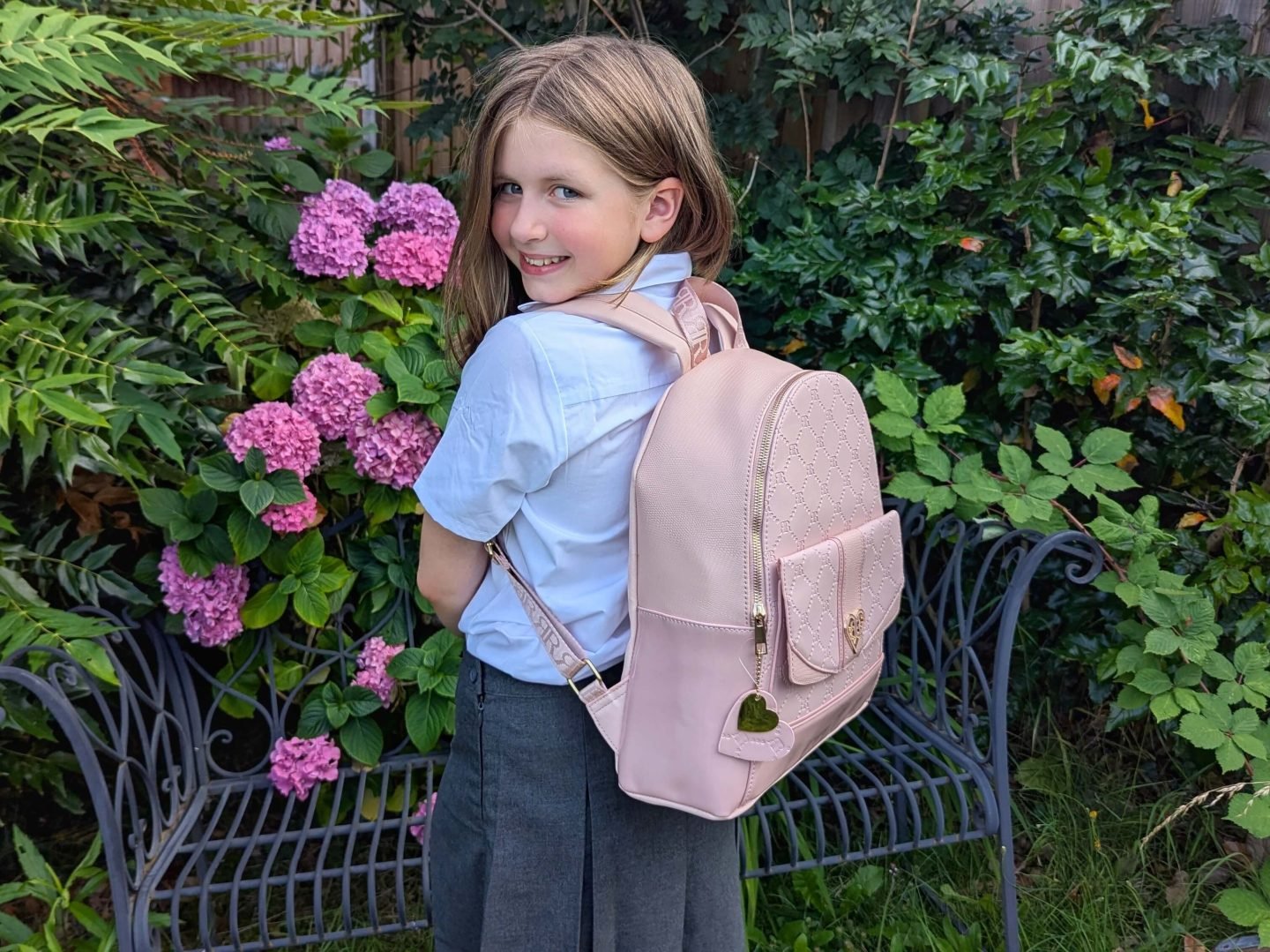 Lia standing in front of a garden bench and hydrangea wearing a pink River Island backpack