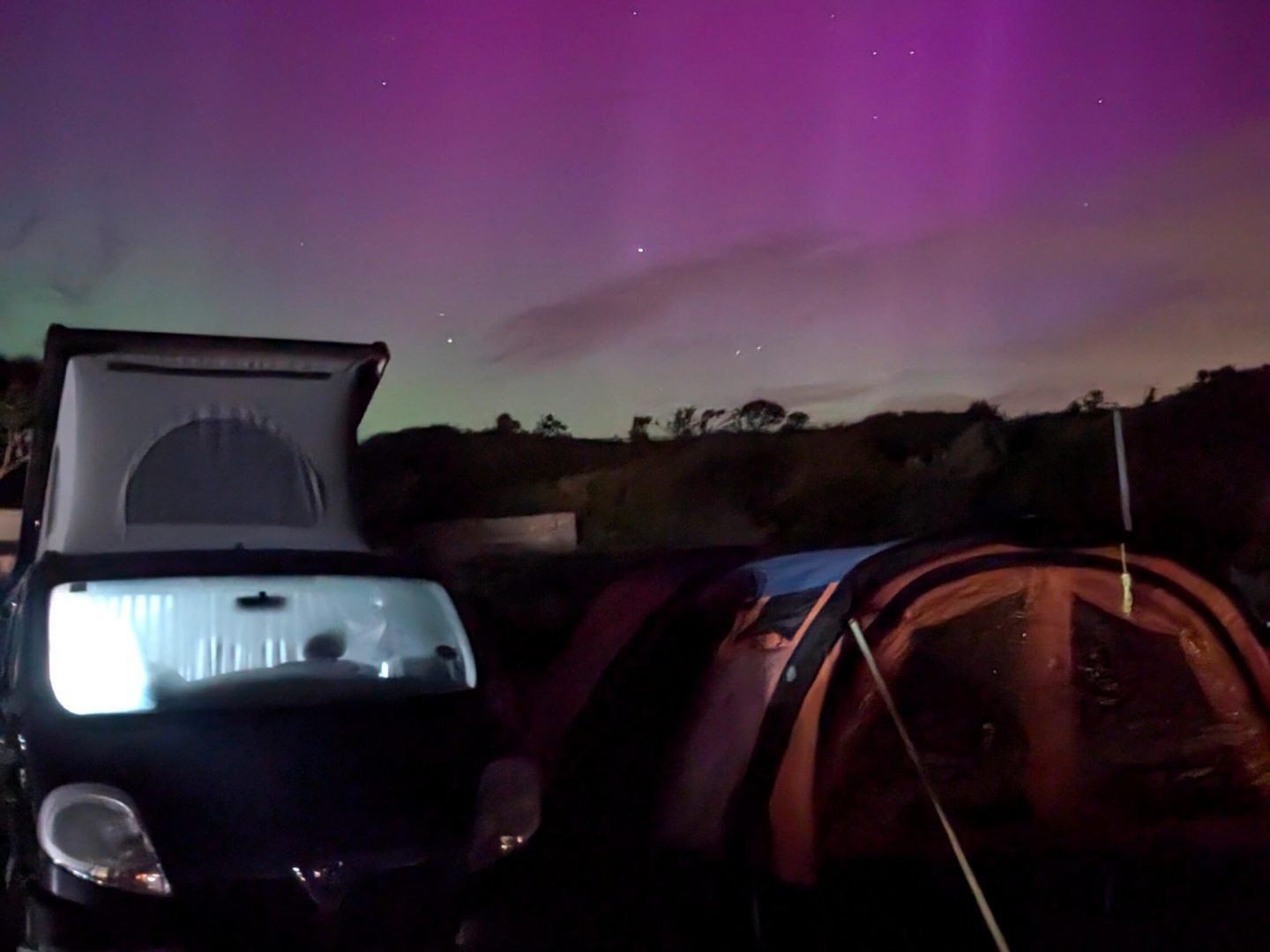 Camper van and awning with aurora borealis behind