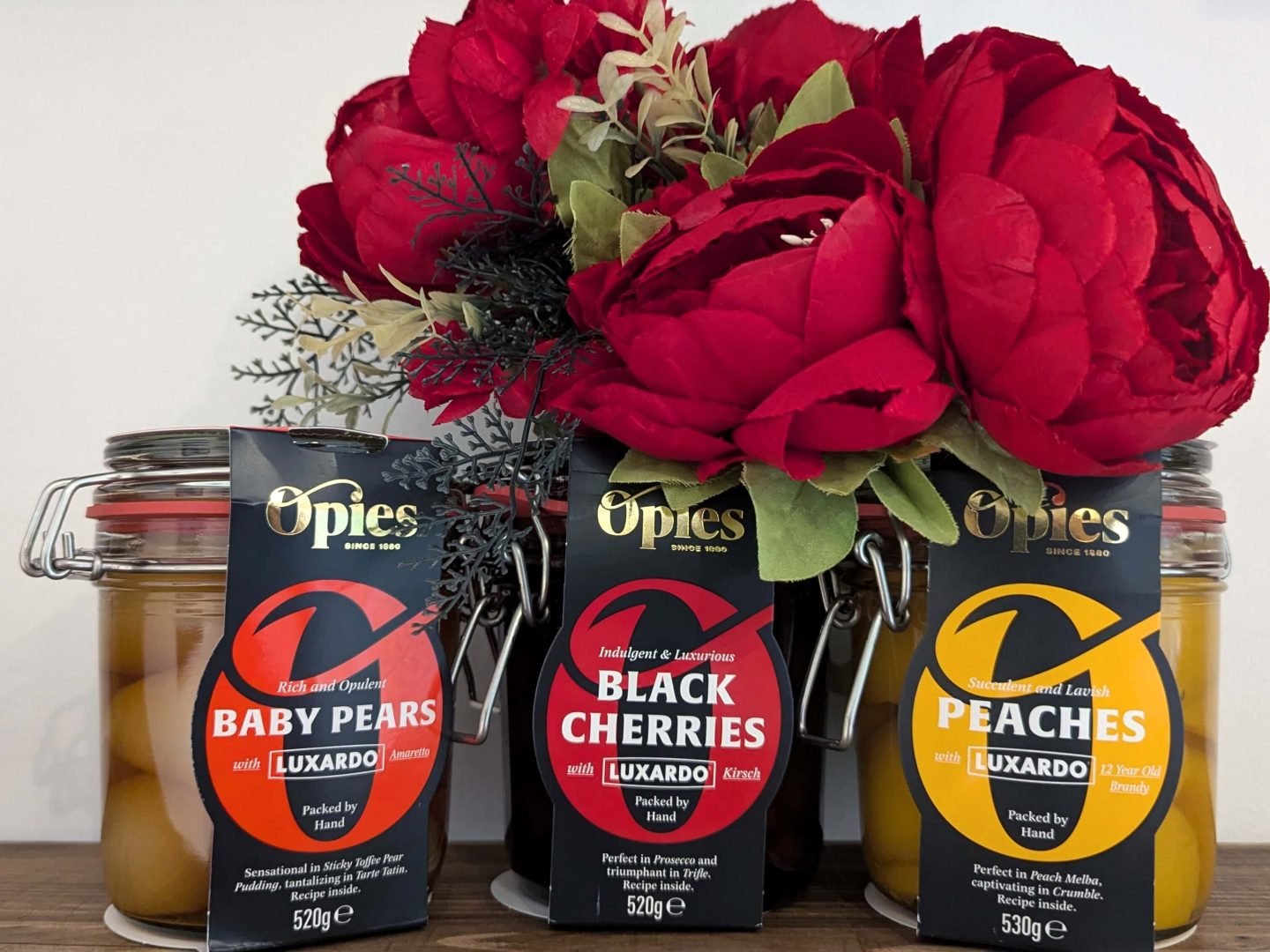 Three Opies fruits in jars - pears, cherries and peaches all in liqueur displayed in front of red  Christmas flowers