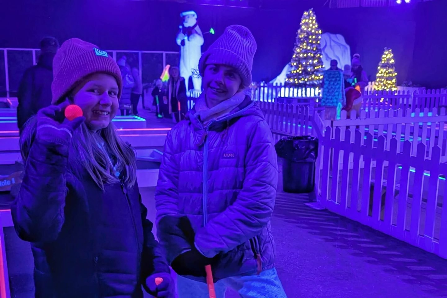 Libby and Lia with their golf clubs in UV crazy golf at Winter Glow Malvern Worcestershire 2025