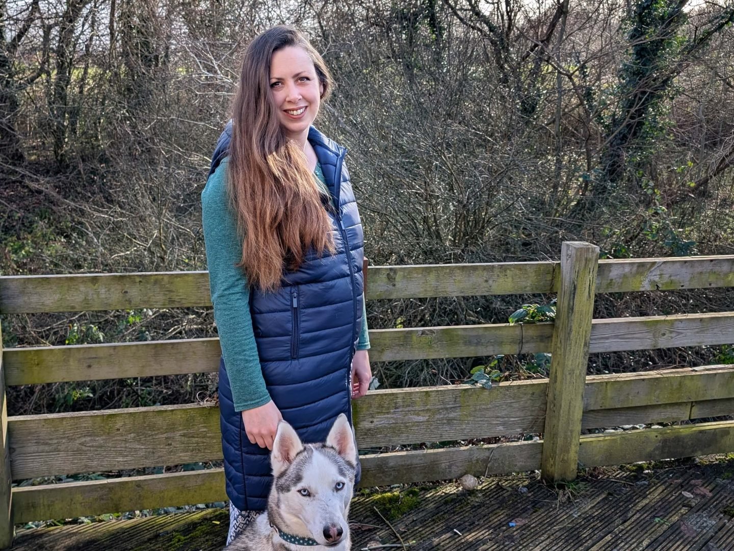 Natalie in a long blue gilet standing next to Alaskan husky Marko