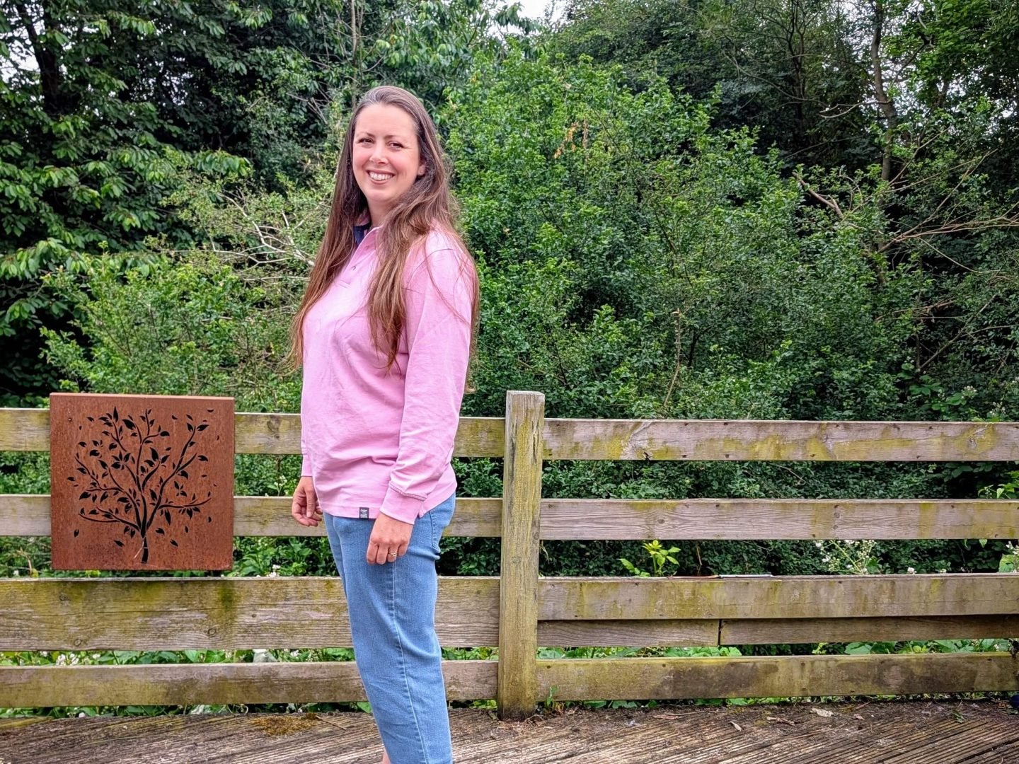 Natalie standing on a wooden decking wearing pink Cotton Traders polo shirt and blue jeans
