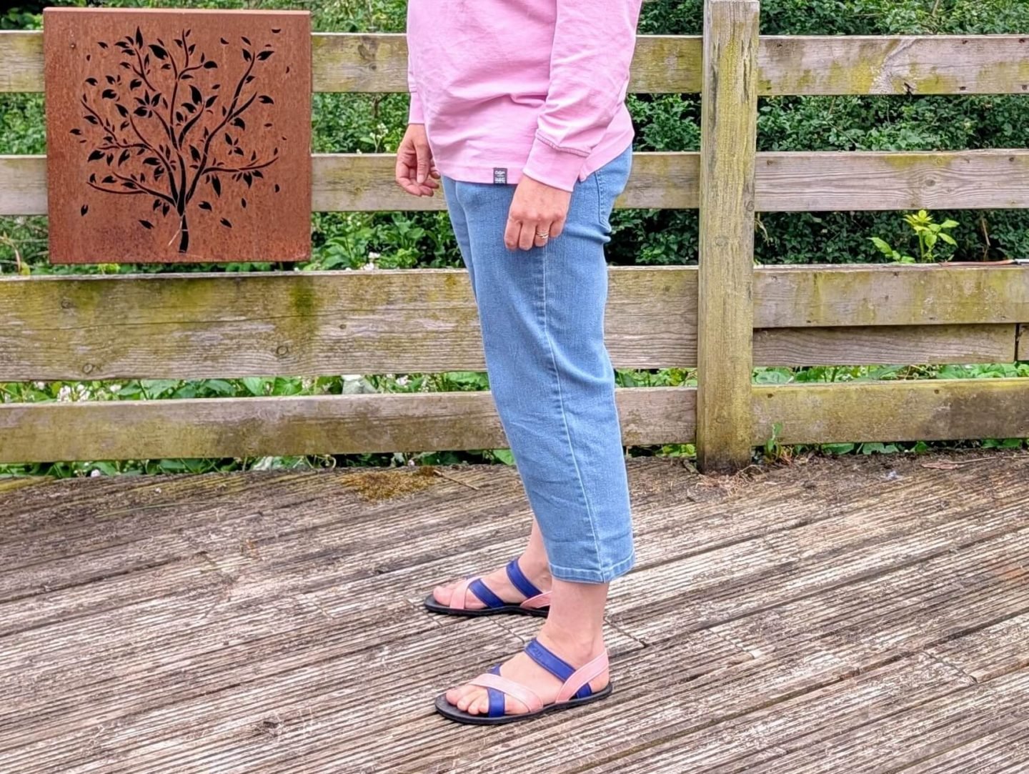 Natalie standing on a wooden decking wearing pink blue jeans, only her bottom half is visible