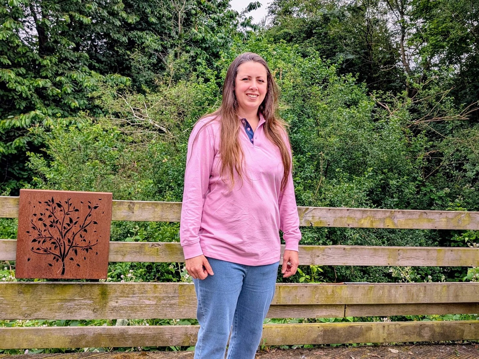Natalie standing on a wooden decking wearing pink Cotton Traders polo shirt and blue jeans