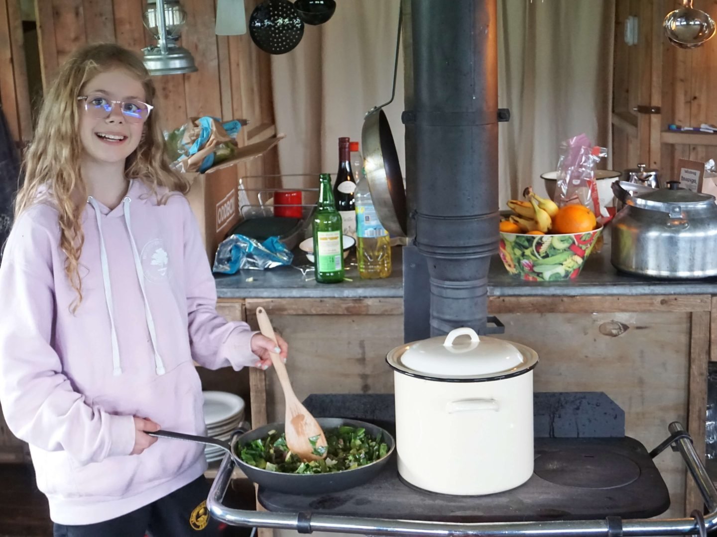 Girl cooking on a wood burning stove at Billingsmoor Farm in a Feather Down glamping canvas hideaway