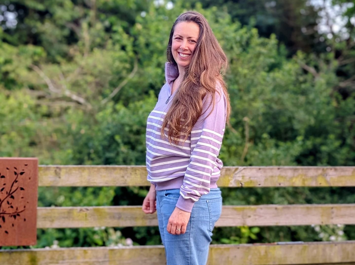 Natalie standing on a wooden decking wearing lilac half-zip Cotton Traders sweatshirt and blue jeans
