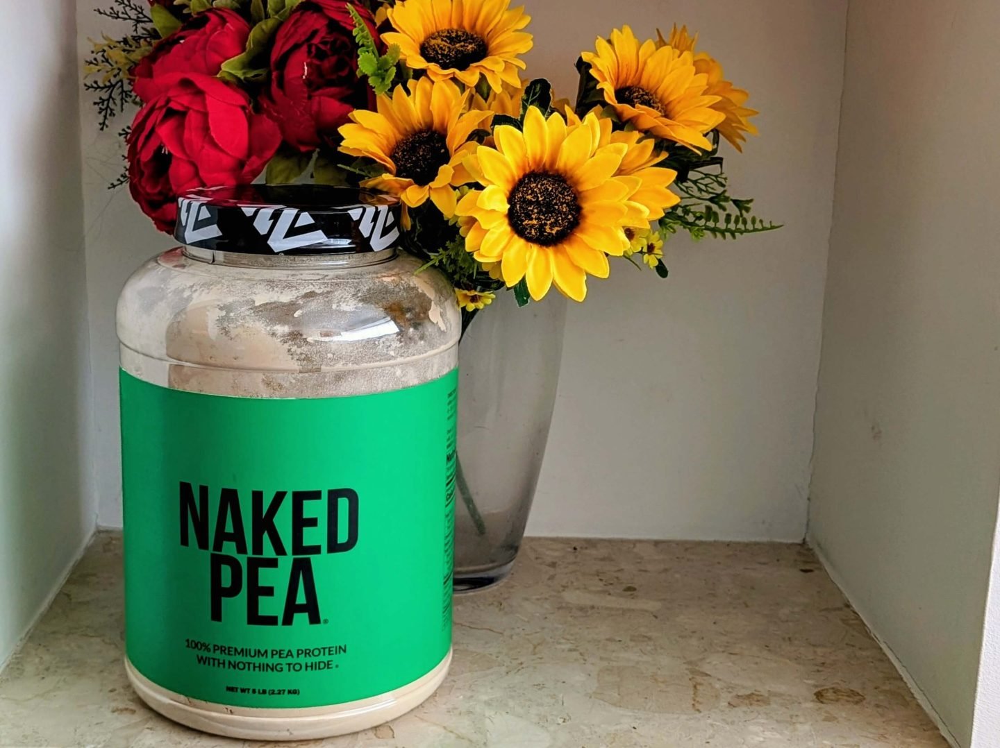Naked Pea protein powder displayed in front of a vase of red and yellow flowers