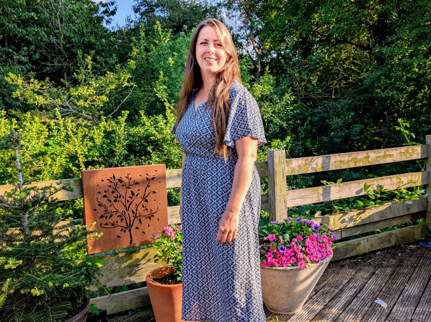 Natalie in a printed maxi dress in front of potted pink flowers in the garden
