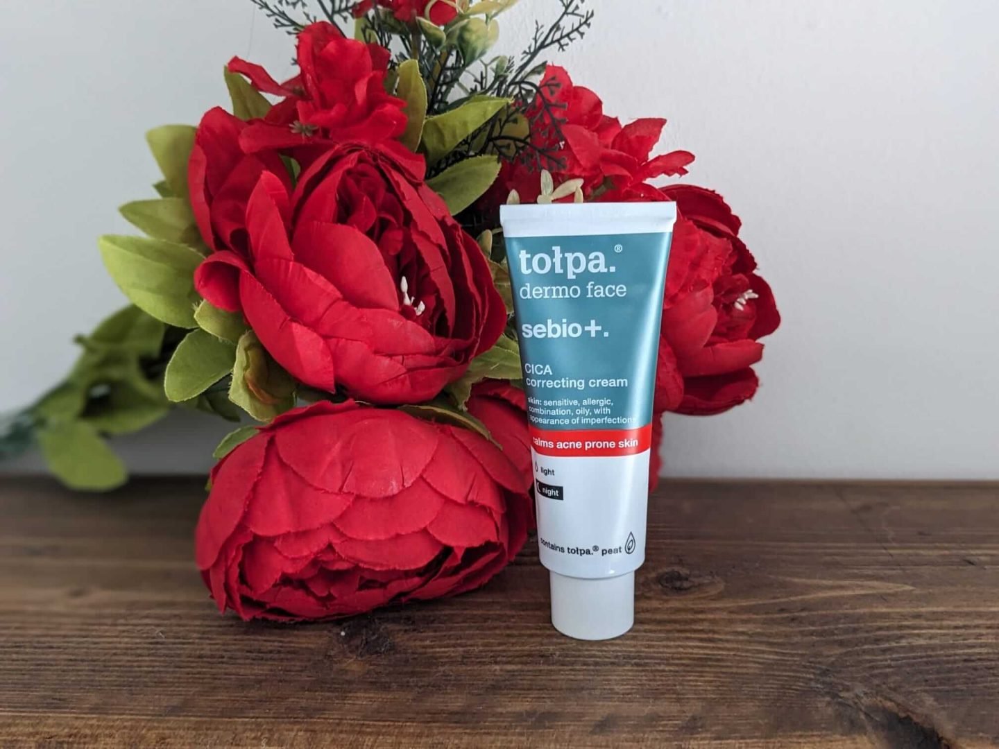 Tolpa Dermo Face correcting cream for teens and tweens displayed against red Christmas flowers on a dark wood shelf