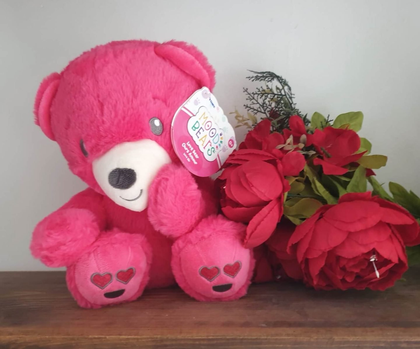 Pink mood bear by red Christmas flowers on a wooden shelf