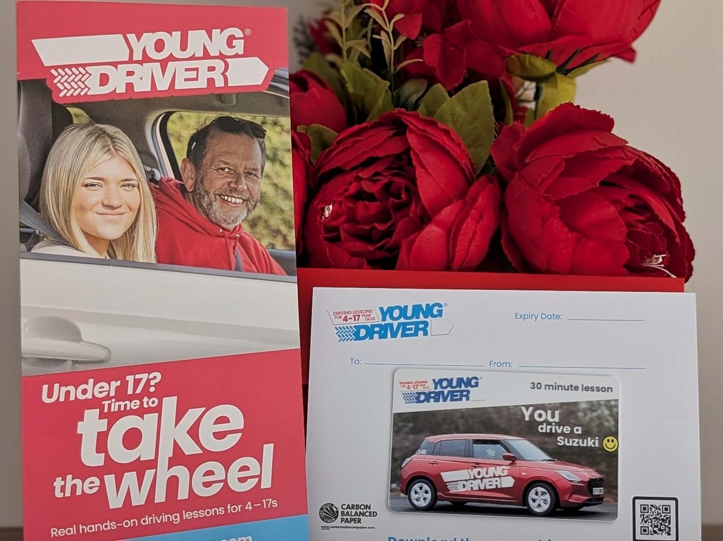 Young driver voucher and leaflet displayed in front of red Christmas flowers