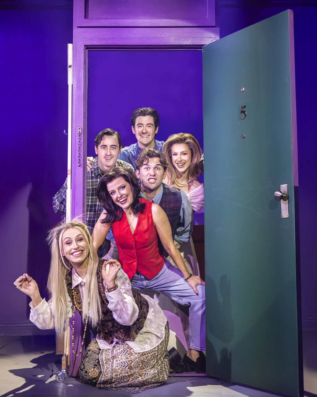 The cast of FRIENDS! The Musical Parody on stage looking through a door