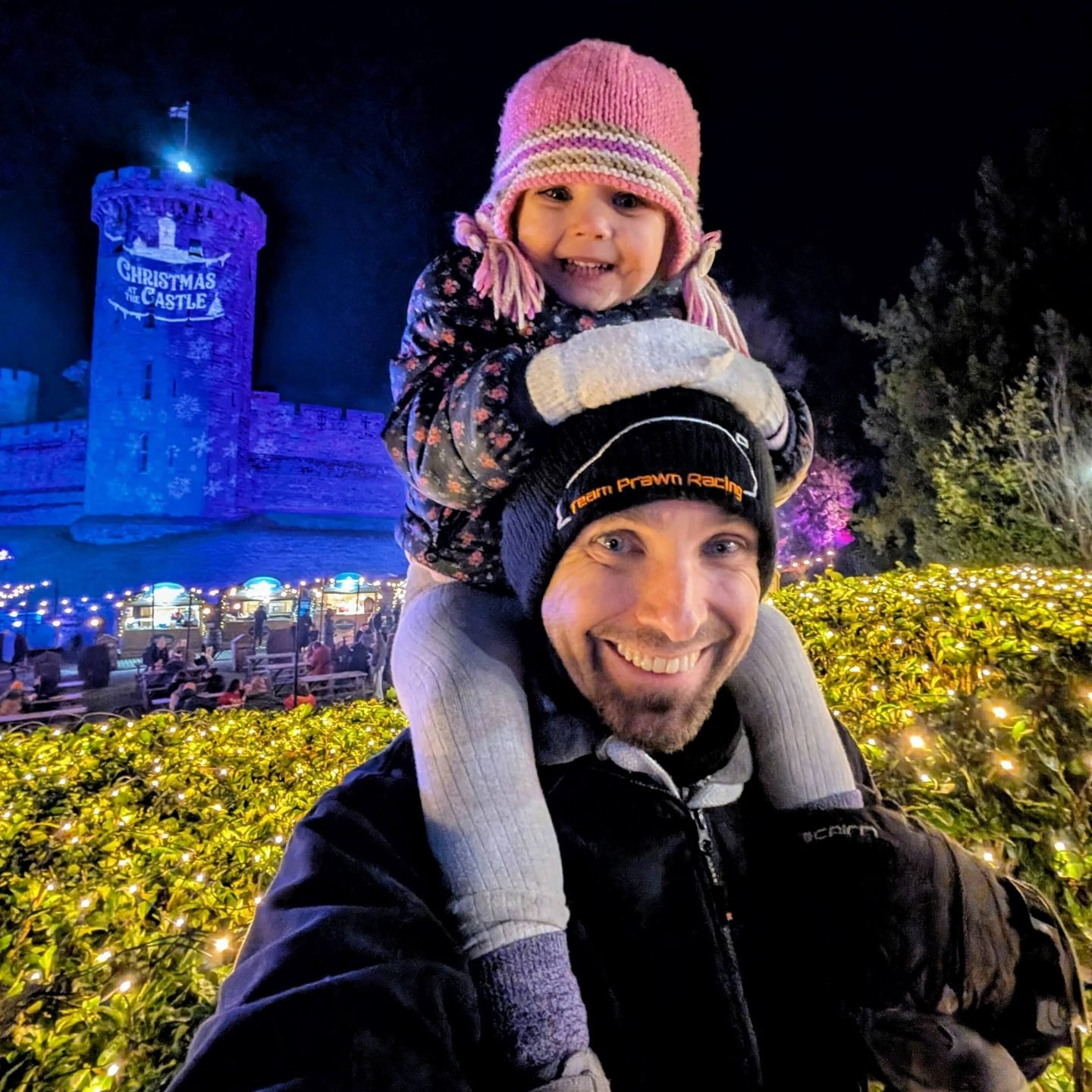 Man with a girl on his shoulders stood outside at Warwick Castle which is lit up for Christmas at the Castle
