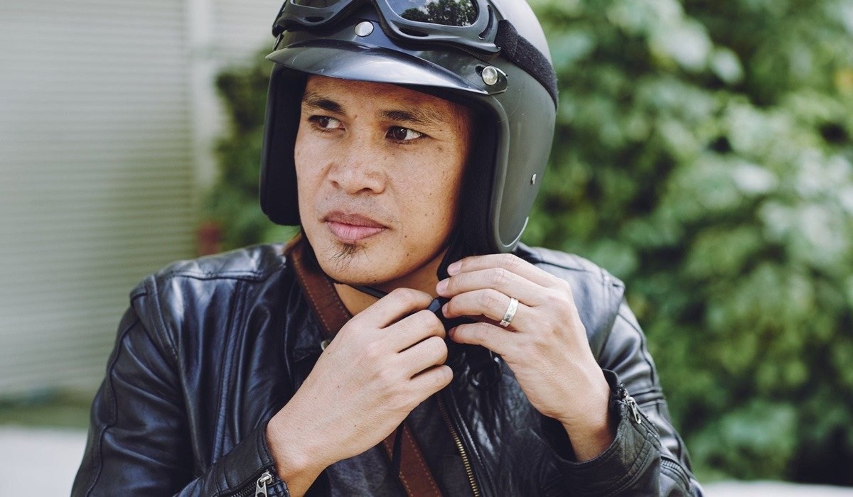 Motorcyclist fastening helmet in leather jacket