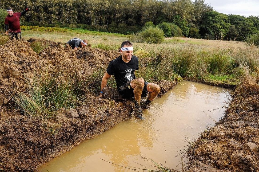 man sitting on grass with feet in muddy water