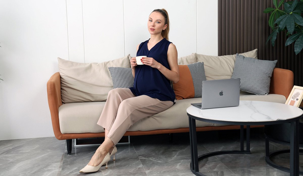 Pregnant woman relaxing on sofa with coffee and laptop