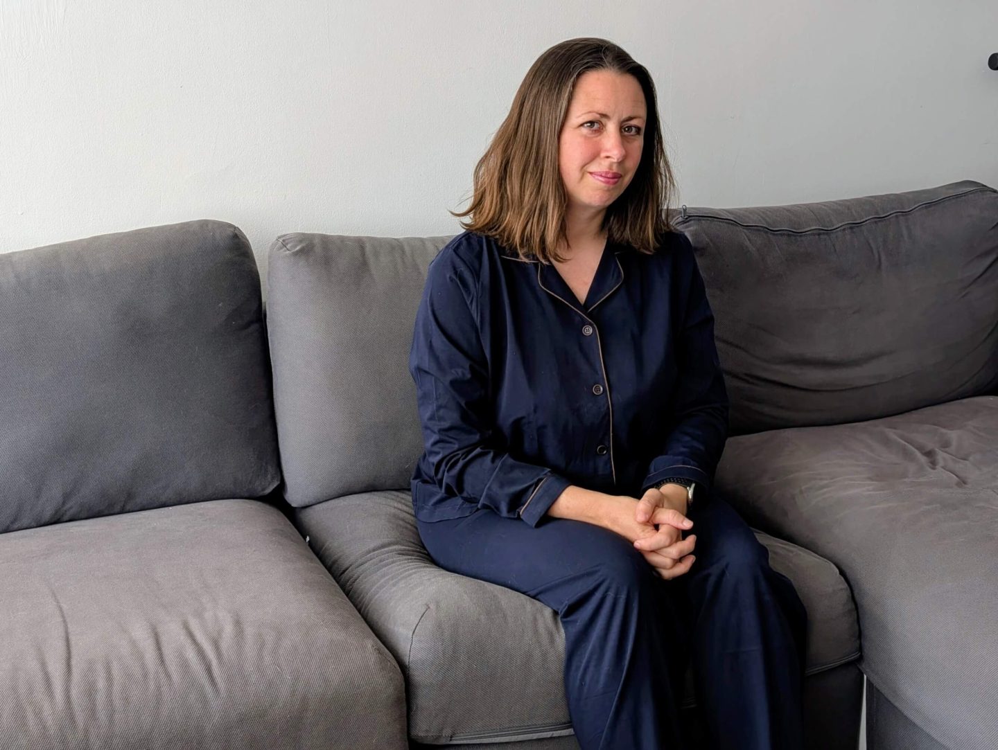 Natalie sitting on a sofa wearing Dark blue copper-infused pyjamas from Copper clothing
