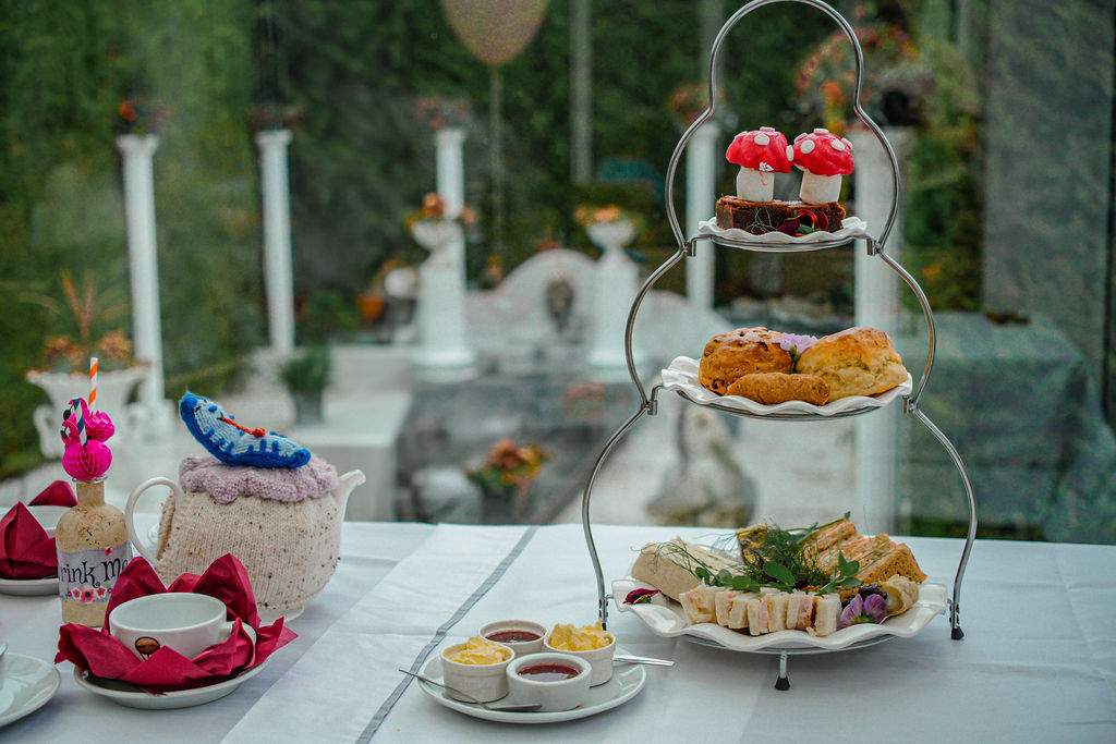 Alice in Wonderland themed afternoon tea at Ralph Court Gardens in Herefordshire, West Midlands image of a three tier afternoon tea with edible sweet toadstools on a chocolate brownie, scones, quiche and sandwiches and a themed tea pot