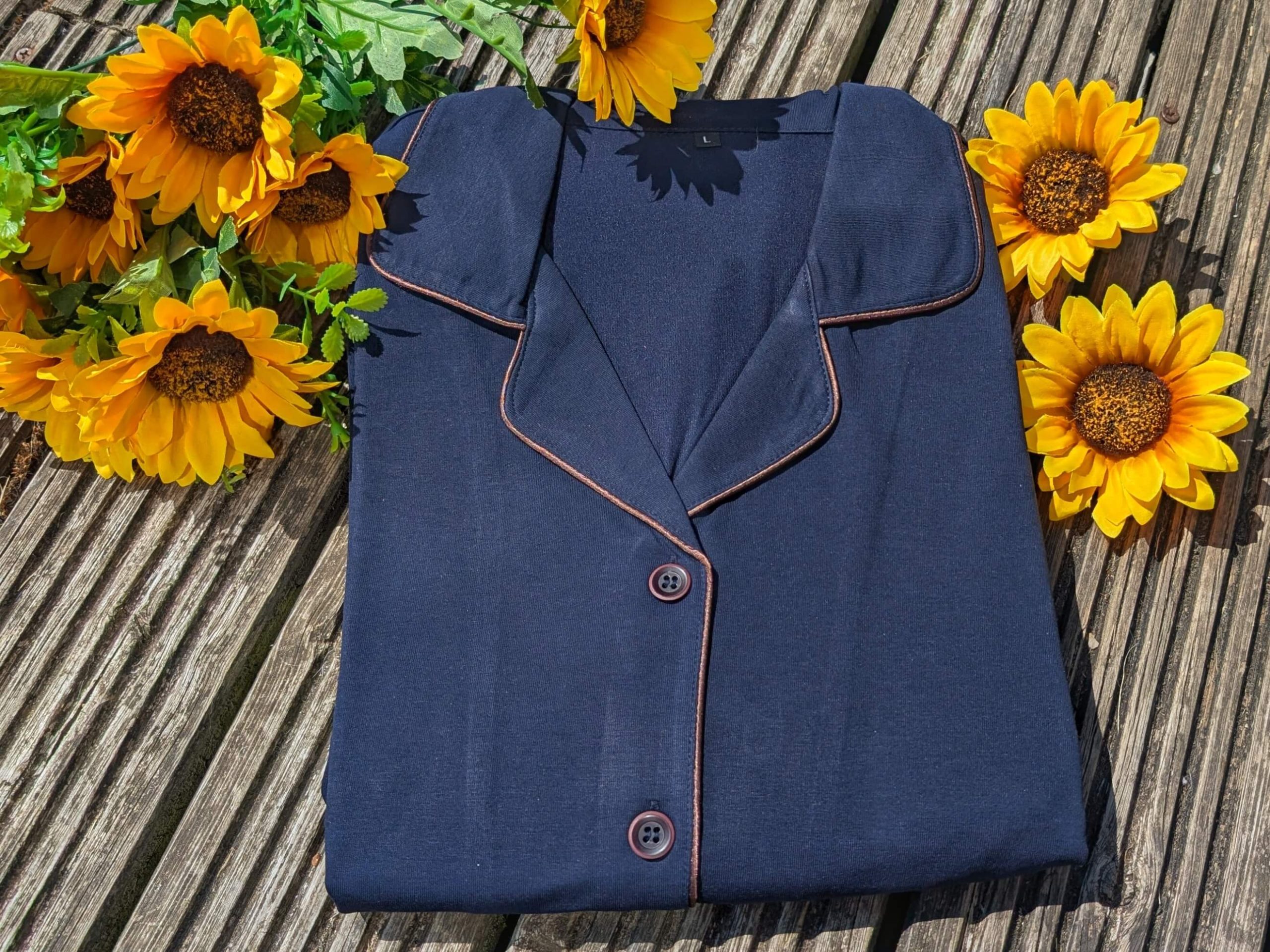 Dark blue copper-infused pyjamas from Copper clothing displayed folded up against wooden decking with sunflowers beside
